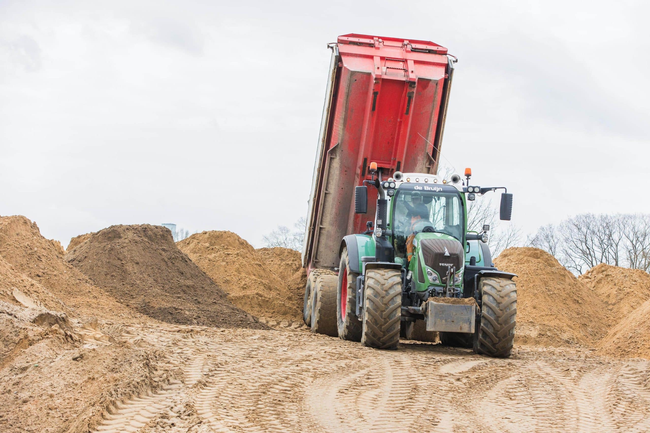 Tractor met kiepwagen stort zand op een bouwplaats