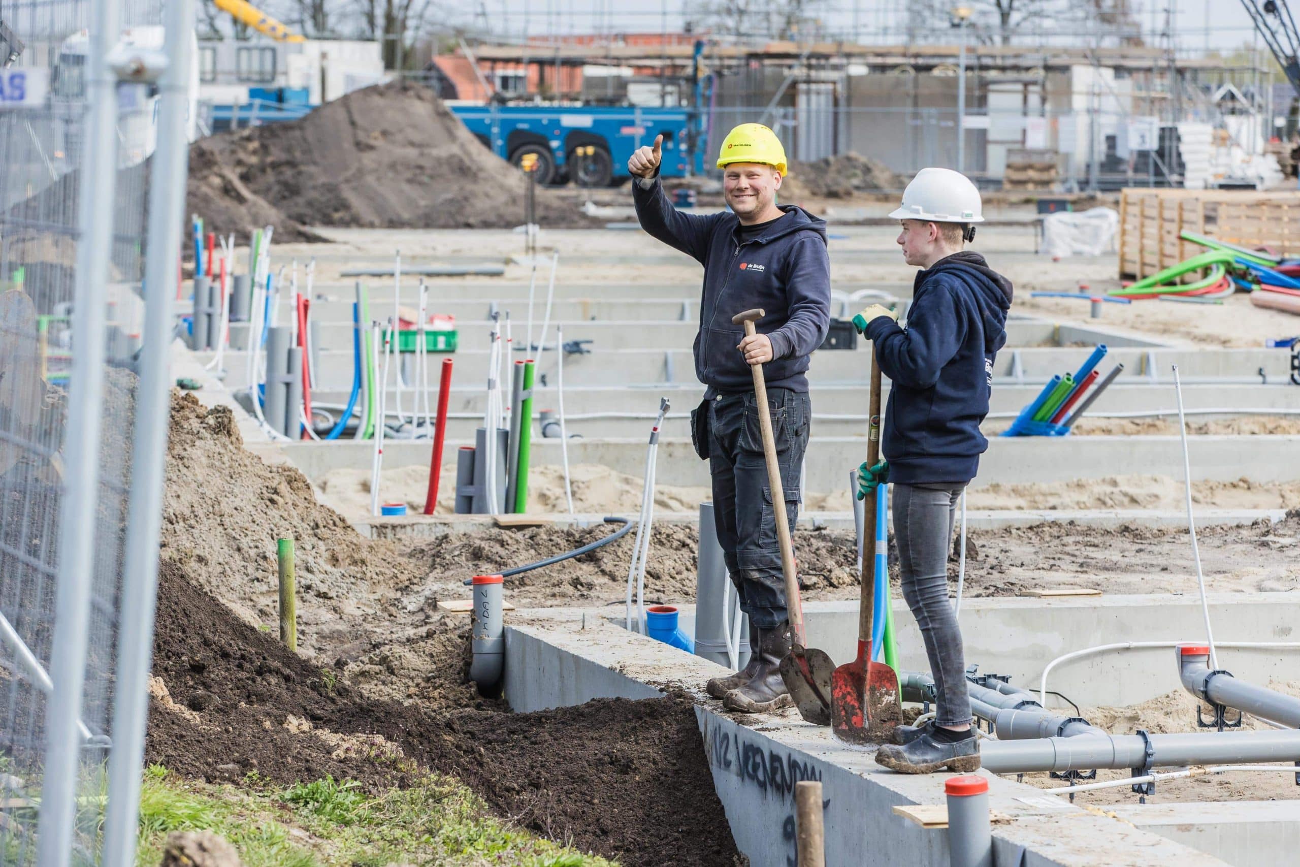 Twee medewerkers aan het werk op een bouwplaats met grond- en leidingwerk